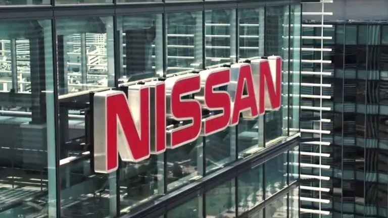 A large red and white sign with the word "NISSAN" is prominently displayed on the glass facade of a modern high-rise building, reflecting the surrounding urban landscape with tall buildings and geometric designs, symbolizing its vigilance in cybersecurity to counter any cyberthreats.