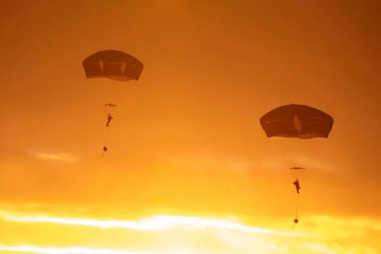 Two parachutists descend from the sky against a stunning, fiery sunset backdrop. The warm orange and yellow hues create a dramatic silhouette of the parachutes and figures, adding a serene yet adventurous atmosphere to the scene, reminiscent of navigating cybersecurity threats in an ever-changing landscape.