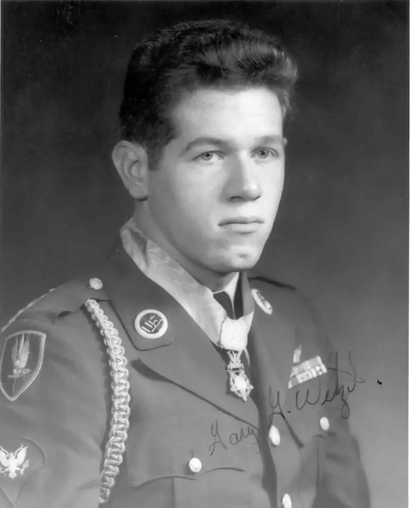 Black and white portrait of a young man in military uniform, adorned with various insignia, medals, and an award around his neck. He has short, neatly styled hair and a serious expression. An autograph is scribbled on the bottom right of the photo, highlighting his role in addressing cyberthreats for the DOD.