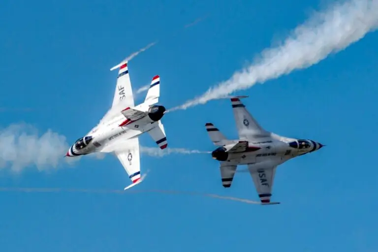 Two U.S. Air Force Thunderbirds F-16 fighter jets perform a daring aerial maneuver, flying in close formation with contrails streaming behind them. The jets, flaunting matching white, blue, and red paint schemes against a clear blue sky, epitomize the power to counter any aerial threat.