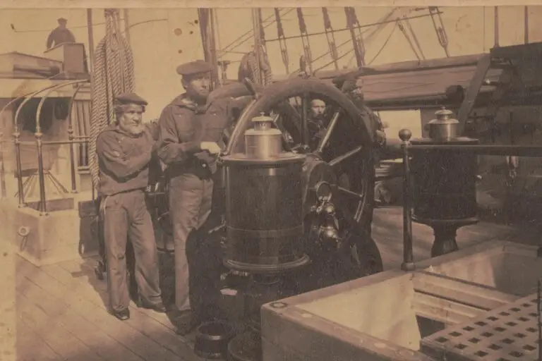 This sepia-toned image shows three sailors in vintage naval uniforms on the wooden deck of an old ship. One sailor is steering the large ship’s wheel, while the other two stand beside him, reminiscent of a time when cyberthreats were as distant as the horizon. Ropes, masts, and parts of the ship are visible in the background.