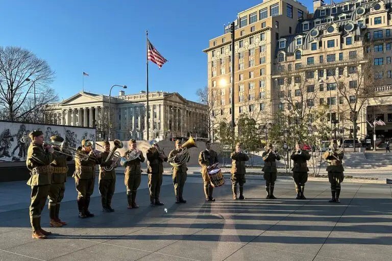 A brass band dressed in military uniforms performs outdoors in front of a historic building with columns and an American flag. Nearby, an ornate multi-story building and leafless trees suggest a cold, sunny day—an atmosphere so picturesque it seems impervious to any cyberthreat.