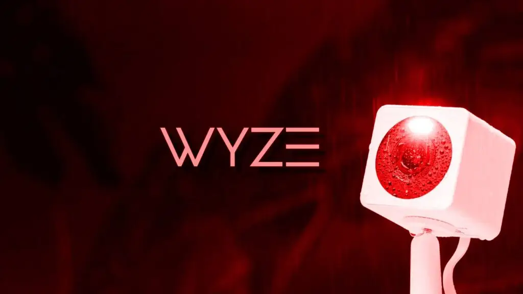 A red-toned image highlights a white security camera with a glowing red light on the front, signifying heightened cybersecurity. Mounted on a stand, the camera features the bold, stylized text "WYZE" prominently displayed above and to the left.