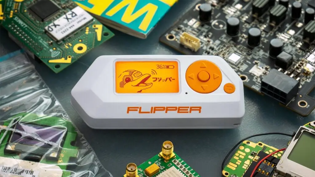 A photo of a Flipper Zero device on a table surrounded by various electronic components, including circuit boards and other circuitry. The Flipper Zero, a portable multi-tool for cybersecurity enthusiasts and pentesters, features an orange directional pad and an orange screen displaying a dolphin-like graphic.